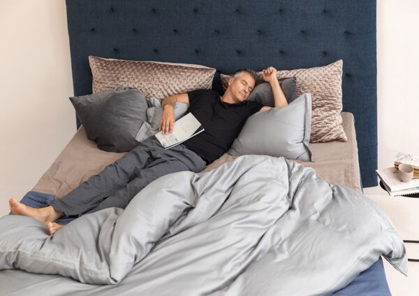 Ein Mann liegt total entspannt mit geschlossenen Augen im Schlafanzug auf einem weichen Bett.